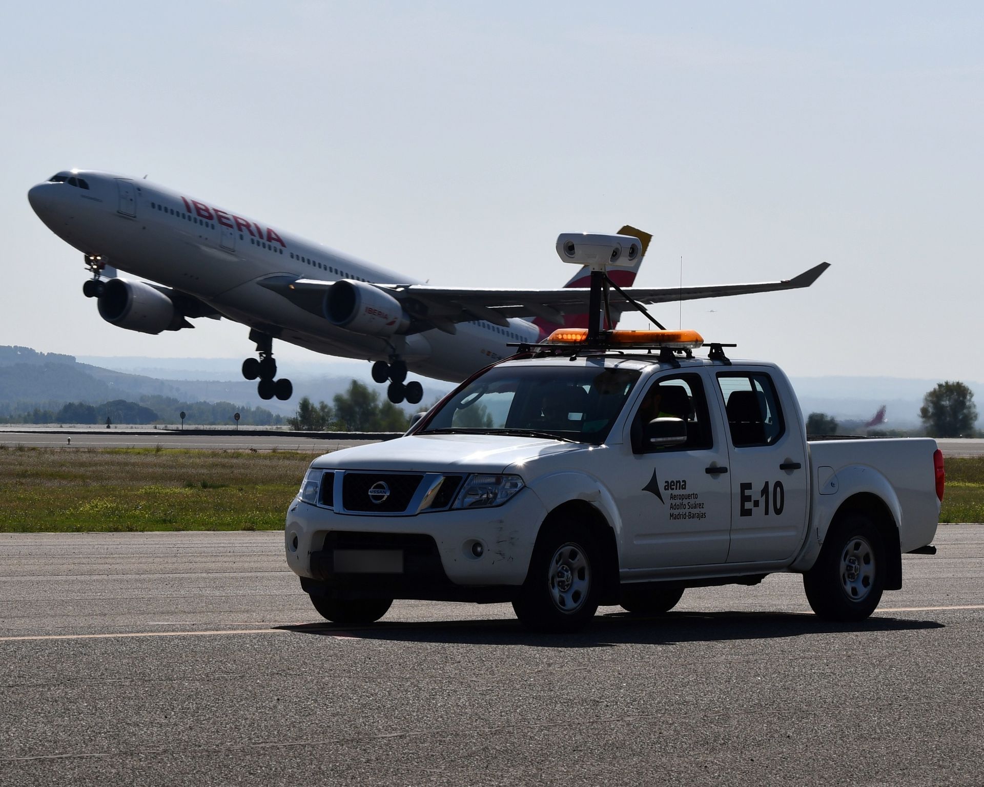 An airliner taking off behind an airport patrol vehicle carrying an Oreyeon sensor unit, in Spain.