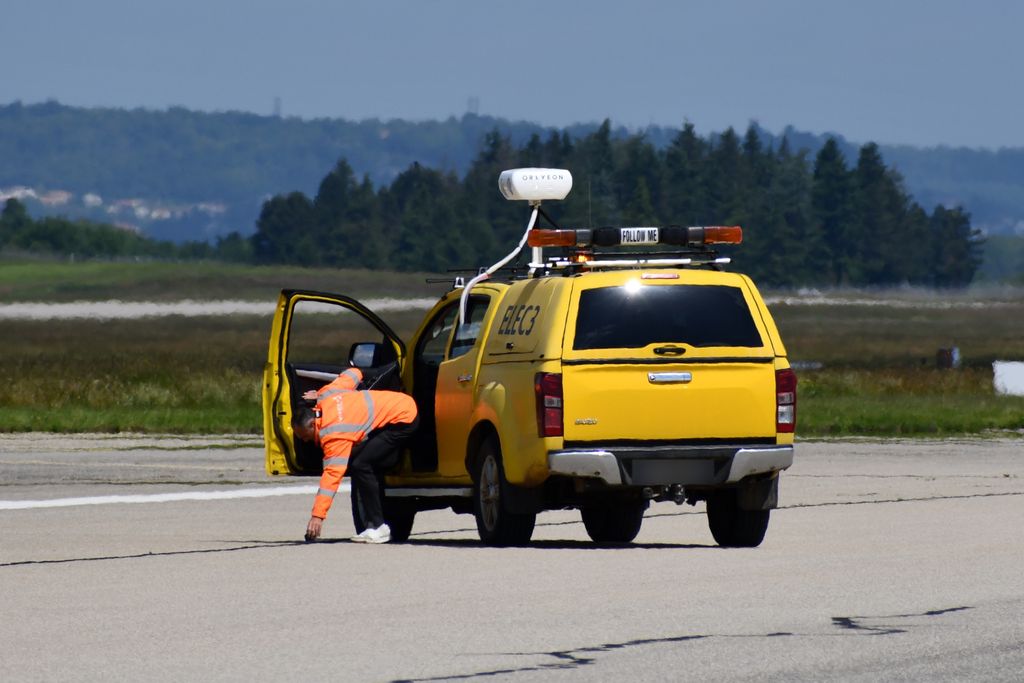 A ground operator in high-visibility clothing retrieving debris beside a Follow Me vehicle carrying an Oreyeon sensor unit, in France.