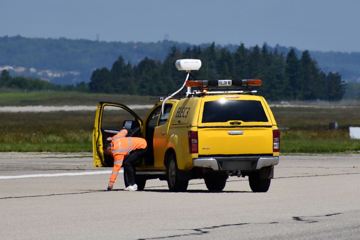 A ground operator in high-visibility clothing retrieving debris beside a Follow Me vehicle carrying an Oreyeon sensor unit.