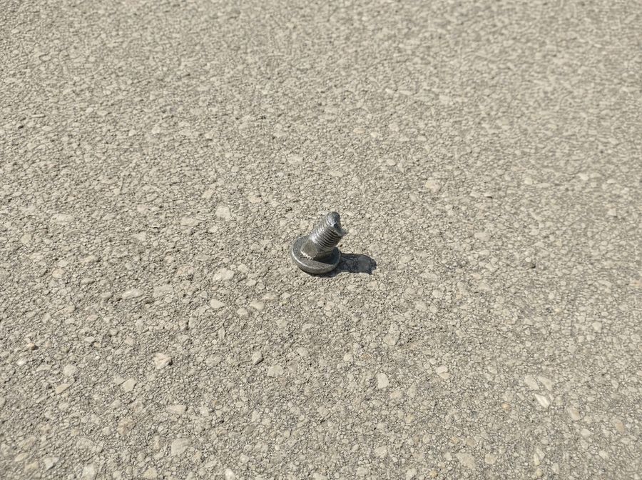A close view of a small metal bolt on coarse runway pavement.